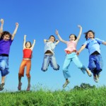 Group of five happy children jumping outdoors.